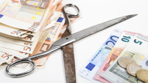 Hur mycket ska det saxas av Lojobornas löner i framtiden? Två högar med eurosedlar och en rostig sax mellan dem.