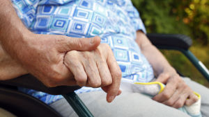 Patienterna ska enligt Jos de Blok skötas så att de inte behöver mer stöd än nödvändigt. En äldre person i rullstol håller en vårdare i handen.