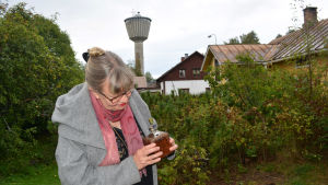 Hemma på gårdsplanen mellan regnskurarna. I bakgrunden det gula huset "Berthas". Ann-Sophie tittar i en kaffekvarn hemma på sin gård. Huset "Berthas" och Nykarleby vattentorn syns i bakgrunden.