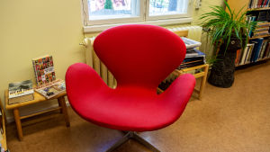 En klassiker. Stolen Svanen formgiven av Arne Jacobsen. Röd stol i bibliotek.