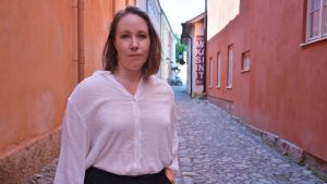 Anna-Stina Hägglund ska föreläsa om pestepidemin i det medeltida Nådendal. En kvinna med axellångt ljusbrunt hår, vit långärmad tröja och svarta byxor står på en kullerstensgata.