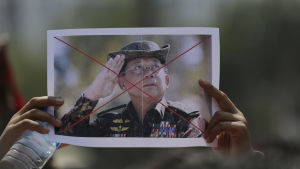 Demonstranter bar på överkryssade porträtt på kuppmakaren general Min Aung Hlaing. Två händer håller upp ett fotografi av den myanmariska kuppmakaren general Min Aung Hlaing. Bilden är överkryssad med rött.
