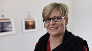 Nykarleby har långa traditioner av ivrigt samarbete mellan konstnärerna och invånarna i staden, säger Tina Nylund Tina Nylund ler mot kameran med foton i bakgrunden.