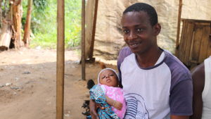 Jean-Jacques med sin dotter. Jean-Jacques sitter utomhus med sin baby i famnen.