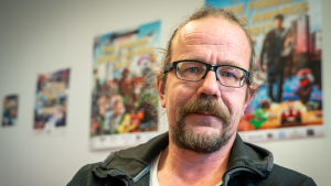 KooPee Hiltunen på Neogames säger att lootlådor måste diskuteras ur ett konsumentskyddsperspektiv. KooPee Hiltunen, direktör för Neogames, tittar in i kameran. I bakgrunden syns planscher på olika spelmässor.