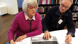 Enter ry:n vertaisneuvoja Raimo Anttila auttaa Irma Pantzaria digipulmissa. Raimo Anttila neuvoo kirjastossa Irma Pantzaria tietokoneen käytössä.