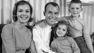 Hä sitter syster och bror och håller god min. Svartvit bild av familj, pappa mamma syster och bror ler mot kameran