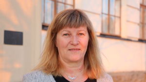 Vicerektor Carina Österback-Ragnäs. En medelålders kvinna med axellångt ljusbrunt hår. I bakgrunden skymtar en gul husvägg och fönster.