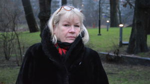 Ros-Mari Djupsund har forskat i gemenskap inom finlandssvensk sång. En blond kvinna iklädd svart jacka står framför ett grönområde.
