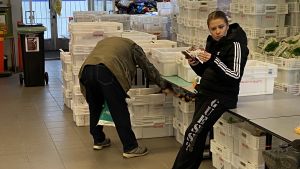 Sini Hursti är verkställande direktör för Hurstin Valinta i Sörnäs. En kvinna lutar mot ett bord och en man böjer sig över en plastlåda med matvaror.