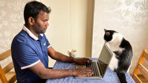 Det blir en hel del sittande framför datorn nu i coronatider. Alla studier ska göras virtuellt nu när skolan håller stängt. En man sitter vid köksbordet och skriver på en bärbar dator. En katt snusar på datorn.