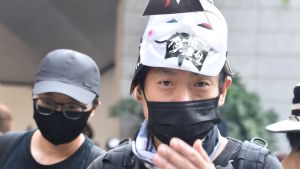 Albert Lai har deltagit i samtliga fredliga demonstrationer. Han säger att han går hem när det bryter ut våldsamheter. Man med andningsskydd ser in i kameran och håller i en iPhone.