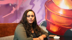 Jasmine anser att det behövs en aktivare diskussion kring rasism i finlandssvenska skolor. Jasmine Kelekay sitter vid ett bord på ett café. Framför sig har hon en kaffekopp och ett vattenglas. Hon tittar leende rakt in i kameran.