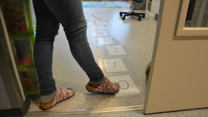 Det har blivit svårare att hitta personal till daghemmen. En barnträdgårdslärare pekar med sin fot på siffror på golvet i en förskola.