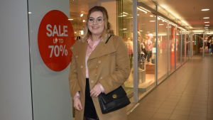 Anna Liljekvist tycker att det finns ett varierat utbud av affärer i Vasa centrum, med både kedjor och mindre affärer. Själv spenderar hon cirka 50-200 euro i månaden på shopping. Kvinna i beige kappa vid reaskylt utanför affär.
