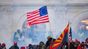 Den federala polisen i USA har hittills gripit över 230 personer som misstänks för att ha varit involverade i attacken. USA:s flagga vajar över en folkmassa framför kongressbyggnaden i Washington. Luften är dimmig av tårgas.