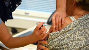 En hälsovårdare vaccinerar en kvinna genom att lägga en spruta i ena armen.