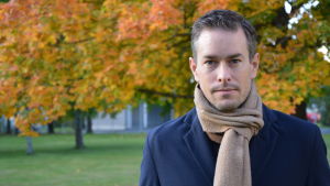 Professor Kim Strandberg. Kim Strandberg, en vit man med halsduk står framför ett träd i höstskrud.
