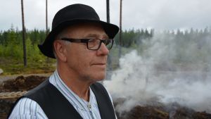 Sven Eklund är rädd att de blir fartblinda och en jakthund får sätta livet till. Arkivbild från tjärbränning i Övermark 2017. Man med hatt, rutig skjorta, väst och glasögon står utomhus.