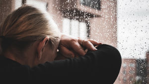 Hormonerna kan ställa till med problem såväl fysiskt som psykiskt. En kvinna lutar sitt huvud mot ett regnigt fönster.