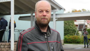 Hangö har haft få coronafall. Det är kanske orsaken till att arbetsplatserna i Hangö är villiga till att ta emot praoelever, funderar studiehandledaren Johan Nilsson. Portättbild på Johan Nilsson, en man med skägg,nästan utan hår på huvudet, klädd i svart skinnjacka. Står ute på en skolgård med några elever i bakgrunden.