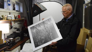 Tapio Kekkonen i sin "man cave" med ett utställningsverk man med tavla i handen i förrådsutrymme
