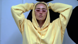 Silvana Imam har sällan långt till känslorna under sina spelningar. Den svenska hiphop-artisten Silvana Imam sitter med händerna bakom huvudet, hon har på sig en gul munkjacka.