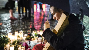 Ung kvinna med mörkt hår spelar på kanteleliknande instrument vid gravljusen och blommorna på Åbo salutorg efter knivdådet den 18.8.2017