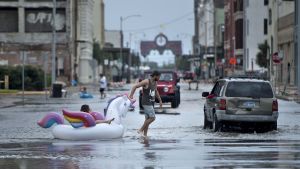 Ett barn och en man tar sig fram bland vattenmassorna i Galveston, Texas den 26 augusti. Ett barn sitter på en uppblåsbar badleksak i form av en enhörning medan en man drar leksaken i vattenmassrona i Galveston, Texas den 26 augusti 2017 efter att orkanen Harvey fört med sig stora regnmängder.