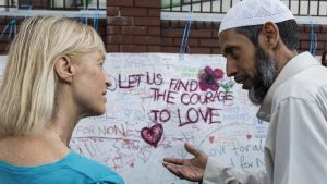 En kvinna och en muslimsk man diskuterar framför en skylt som uppmanar till kärlek och samverkan. En kvinna och en muslimsk man diskuterar framför en skylt som uppmanar till kärlek och samverkan.