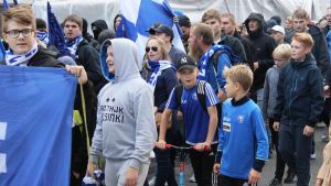 Direkt bakom de maskerade HJK-anhängarna går barn. HJK-supportrar från Klubipääty marscherar till derbyt mot HIFK. Flera av anhängarna är barn.