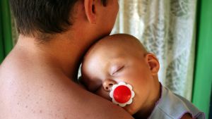 Spädbarn kan få svåra symptom av RS-viruset. Baby sover med huvudet på sin pappas axel.