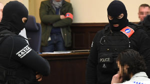 Salah Abdeslam (till höger) sitter omringad av belgiska specialstyrkor i rättegångssalen under rättegångens första dag. Den huvudmisstänkta Salah Abdeslam (till höger) sitter omringad av belgiska specialstyrkor i rättegångssalen strax innan rättegången ska inledas.