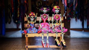 värikkäästi puetut luurankonuket istuvat penkillä, yksi tuulettaa riemukkaasti