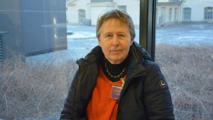 Tiina Torkkeli-Pitkärantas släkt är från Karelen. tiina torkkeli-pitkäranta sitter framför ett fönster och tittar in mot kameran.