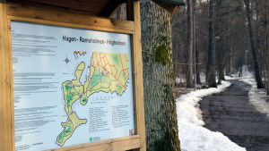 Ramsholmen är ett populärt ställe att besöka även bland hundägare. Det ligger intill området där den nya hundparken planeras. En informationsskylt där det står Hagen-Ramsholmen-Högholmen ovanför en karta. Till höger om skylten syns en stig.