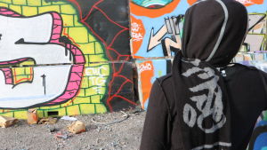 Kim tycker att straffen för graffiti är oproportionerliga. En person står framför en vägg målad med graffiti.