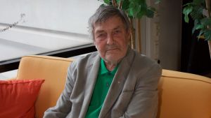 Claes Andersson titulerar sig idag pensionär. Claes Andersson sittande i orange soffa - 2018.