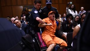 En högljudd demonstrant i orange fångdräkt avlägsnas ur salen. En högljkudd demonstrant i orange fångdräkt avslägsnas av flera poliser från kongressen