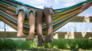 Sommarvärmen är här, lämpligt till skolavslutningarna. Två barn ligger i en hängmatta.