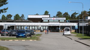 Hälsocentralen i Kristinestad. En sjukhusbyggnad i bakgrunden. Fram i bilden en parkeringsplats med flertal bilar.