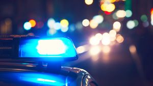 En polisbils blåljus lyser i natten med gatulyktor och billjus i bakgrunden.