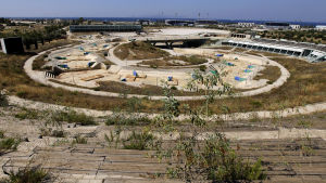 Kajak- och kanotstadion i Aten tio år efter OS 2004. en övergiven kajakstadion i aten. en tom betongränna med hinder i sig. det växer ogräs överallt.