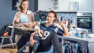 Melk. Kaksi naista istuu vauva sylissä keittiössä ja katsoo kameraan. Takana näkyy mm. viinipullo.