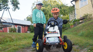 Emil Roos ska köra bilen medan brorsan Elis Roos (till vänster) är "servicekarl" som han själv kallar sig. Längst fram på bilen finns en tecknad grävling - på den står det Emil. En pojke sitter på en lådbil. Brevid honom står hans bror. Pojkarna sitter i en backe på en gård med äppelträd.