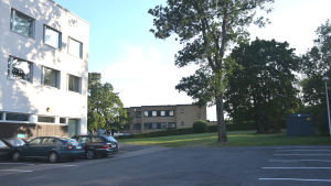 Nuvarande parkeringsplats vid den tomt i hörnet av Stationsvägen och Skillnadsgatan där det skulle byggas ett nytt hus. En parkeringsplats och ett hus.