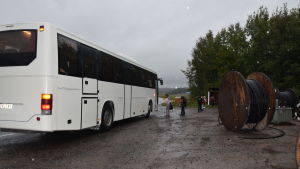 Arkivbild på skoltransport i Raseborg. En vit buss står vid en busshållplats och tar upp passagerare. Skolbarn. Det är ganska mörkt och regnigt.