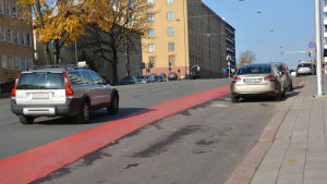 Parkeringsplatser till höger - cykelfil till vänster. Bilar och ett rött körfält för cyklister.