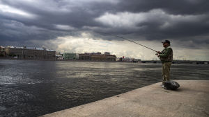 Man som svirvlar vid Nevaflodens strand i St Petersburg. Man som fiskar från stranden av floden Neva i St Petersburg.
