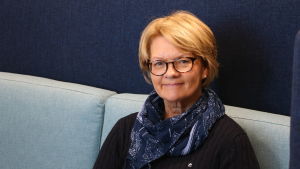 Rektor Åsa Sandgärds. En medelålders kvinna sitta i en blå soffa. Kvinnan har halvlångt ljust hår och glasögon på huvudet. Runt halsen har hon en blå halsduk.